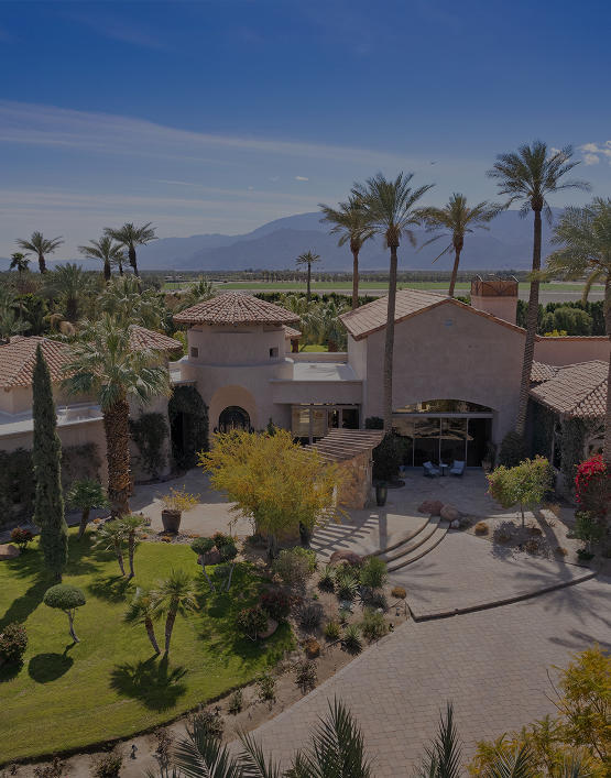 Desert valley landscape with rugged mountains and clusters of palm trees under a clear sky, representing the Coachella Valley setting