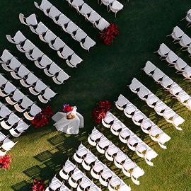Aerial view of wedding ceremony seating arranged in angled rows on green lawn with red floral accents at the altar.