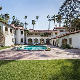 Spanish-style estate with courtyard pool, palm trees, and manicured lawn under blue sky.