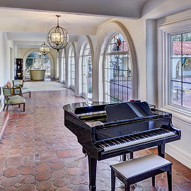 Elegant arched hallway with terracotta tile floor, black grand piano, chandelier, and large windows.