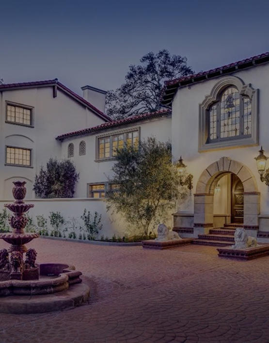 Spanish-style luxury estate home with a red tile roof, palm trees, and manicured grounds