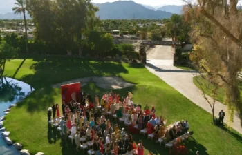 Outdoor wedding ceremony with seated guests on a green lawn near a pond, surrounded by trees, with mountains visible in the background.