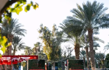Mirrored panels with red accents and flowers stand on a grassy lawn, surrounded by palm trees under a clear sky.